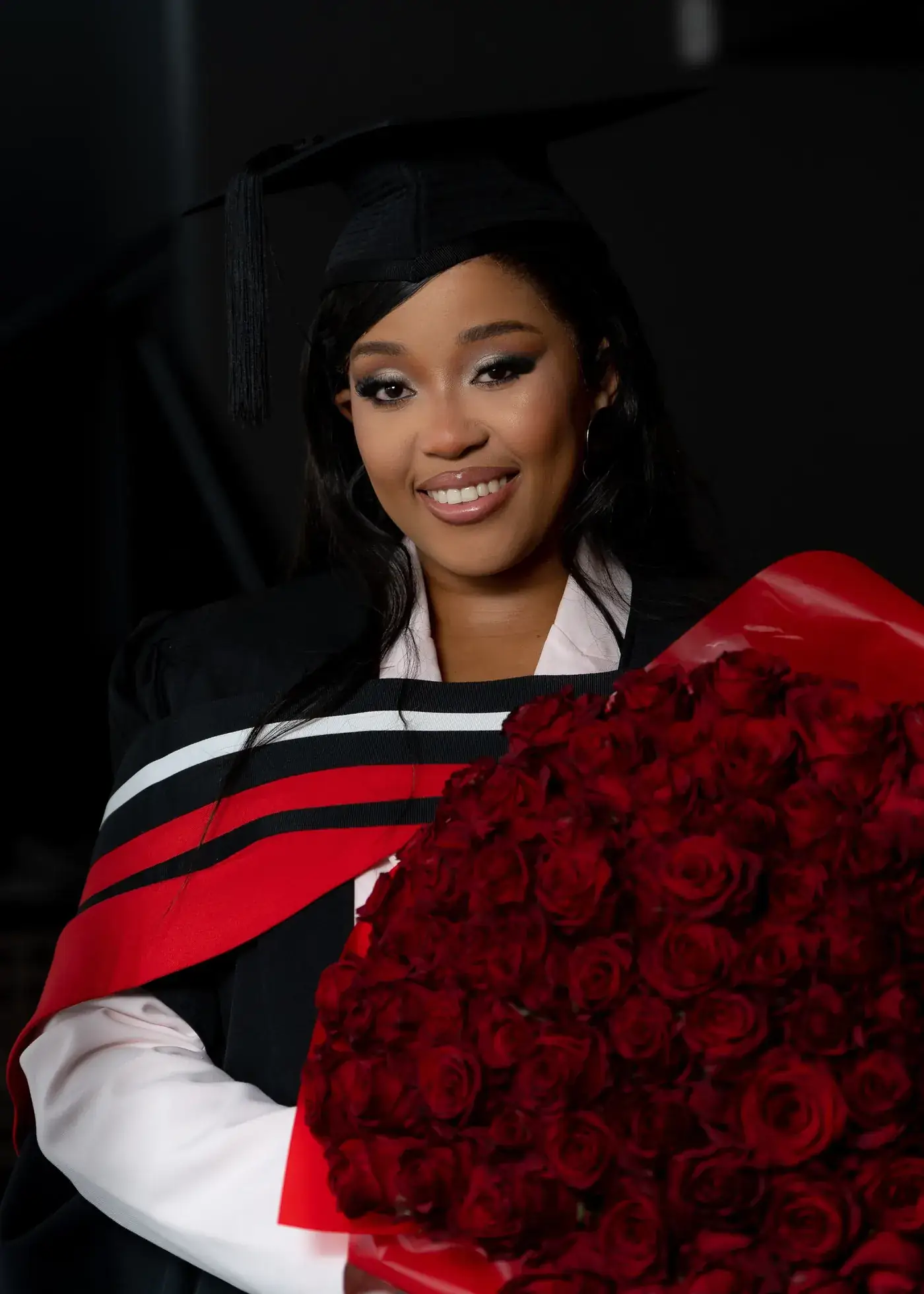 Graduate in cap and gown holding a bouquet of red roses